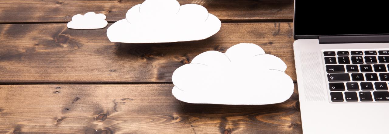 Laptop on Wooden Background with Paper Clouds