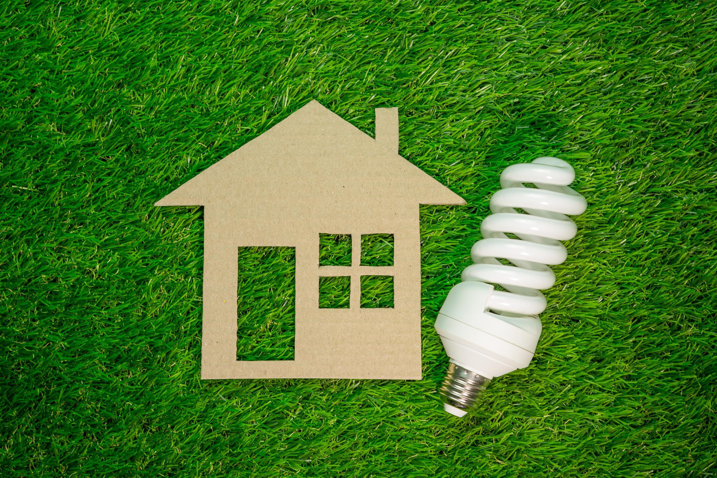 Cut-out paper home next to a CFL light bulb on a grass background