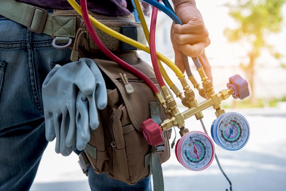 Technician holding HVAC gauge while wearing toolbelt Hand holding HVAC maintenance equipment